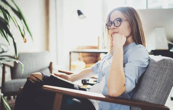 Stilig ung blondin bär glasögon och använder elektronisk touch tablett dator på soliga arbetsplatsen. Horisontella. Suddig bakgrund. — Stockfoto