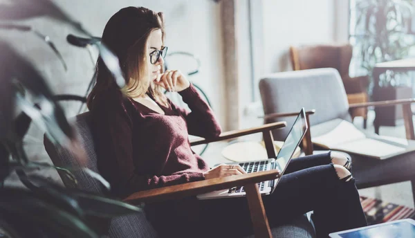 Jovem empresária atraente vestindo roupas casuais e trabalhando no escritório de co-trabalho.Feminino usando laptop móvel contemporâneo enquanto se senta em poltrona conforto . — Fotografia de Stock