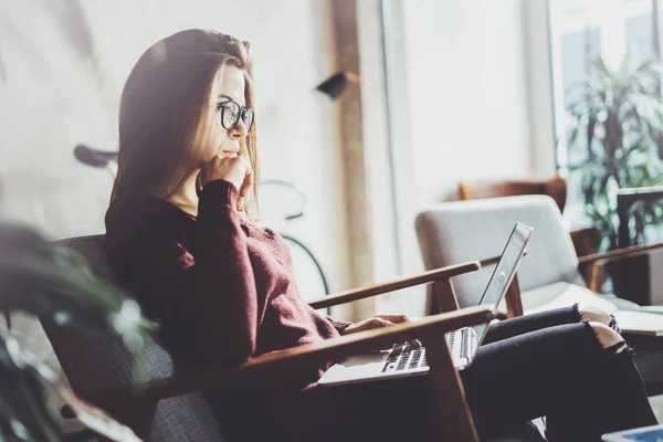 Jovem empresária atraente vestindo roupas casuais e trabalhando no escritório de co-trabalho.Feminino usando laptop móvel contemporâneo enquanto se senta em poltrona conforto . — Fotografia de Stock