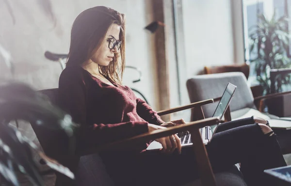 Aantrekkelijke jonge zakenvrouw dragen casual kleding en werken bij coworking office. Vrouw met behulp van de hedendaagse mobiele laptop zittend in comfort-fauteuil. — Stockfoto
