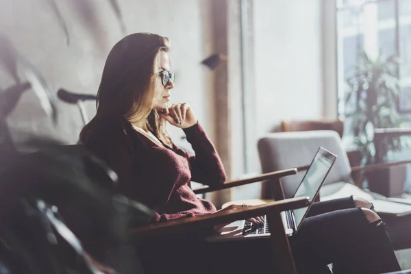 Atractiva joven empresaria que usa ropa casual y trabaja en la oficina de coworking. Mujer que usa un portátil móvil contemporáneo mientras está sentada en un sillón de confort. . —  Fotos de Stock