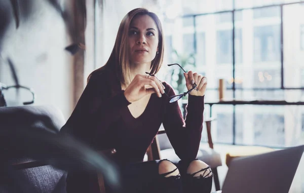 Närbild bild av ung vacker kvinna sitter på en bekväm fåtölj och använder bärbar dator. Arbetar process på coworking studio. Horisontell, suddig bakgrund. — Stockfoto