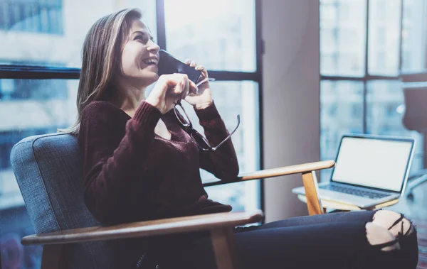 Attraktiv ung affärskvinna talar med partner via modern telefon medan du sitter i comfort fåtölj på modernt mötesrum. — Stockfoto