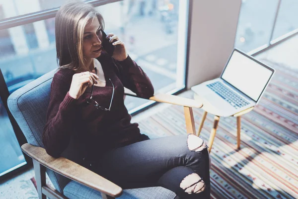 Konfor koltuk modern toplantı odasında otururken ortak modern telefonla konuşurken çekici genç iş kadını.