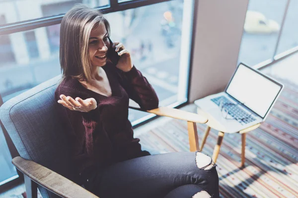 Konfor koltuk modern toplantı odasında otururken ortak modern telefonla konuşurken çekici genç iş kadını.