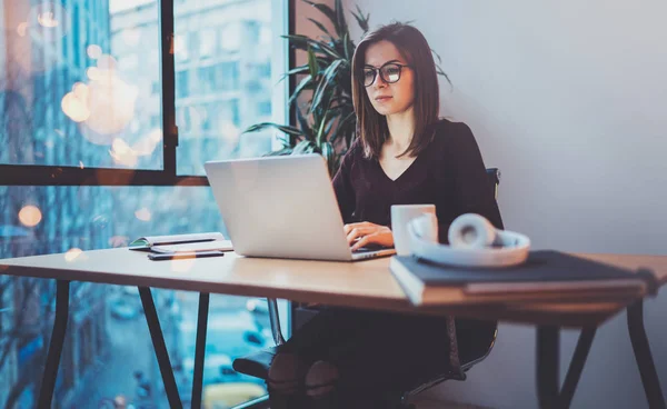 Attraktiva flicka som bär glasögon som arbetar på bärbar dator på sin arbetsplats på natt kontor. Horizontal.Blurred bakgrund. Nödraketer. — Stockfoto