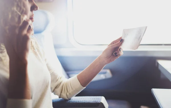 Bénéficiant d'un concept de voyage d'affaires. Jeune belle fille touristique brune voyageant dans le train assis près de la fenêtre à l'aide d'un smartphone, tenant les mains de billets . — Photo