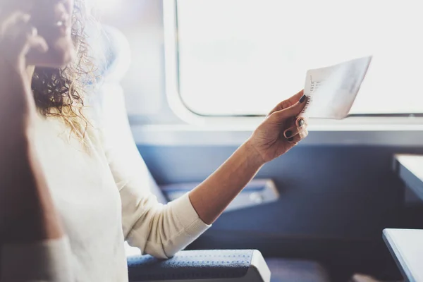 Bénéficiant d'un concept de voyage d'affaires. Jeune belle fille touristique brune voyageant dans le train assis près de la fenêtre à l'aide d'un smartphone, tenant les mains de billets . — Photo