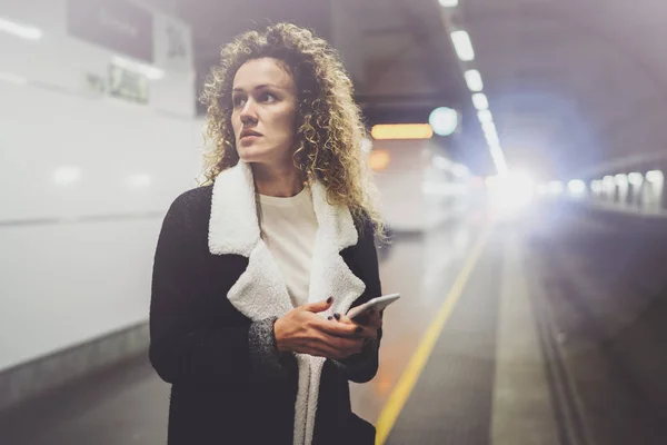 Mooie vrouw op pendelen doorgang met behulp van smartphone terwijl je in de treinstation. Aantrekkelijk meisje gelukkig met mobiele telefoon app voor gesprek in vakantiereizen. — Stockfoto