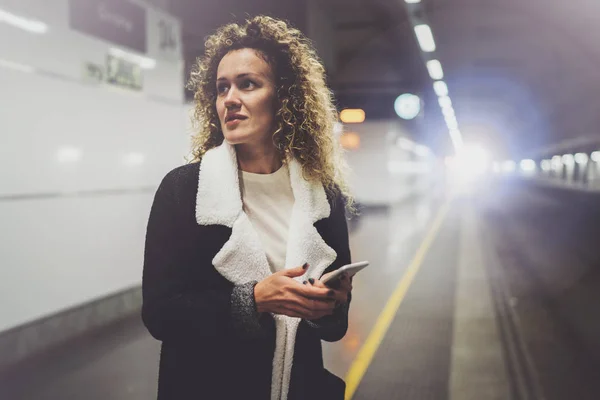 Mooie vrouw op pendelen doorgang met behulp van smartphone terwijl je in de treinstation. Aantrekkelijk meisje gelukkig met mobiele telefoon app voor gesprek in vakantiereizen. — Stockfoto