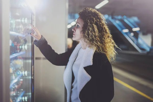 Attraktiv kvinna på transit platform med en varuautomat för moderna dryck. Hennes hand placeras på knappsatsen och hon ser på skärmen liten display. — Stockfoto