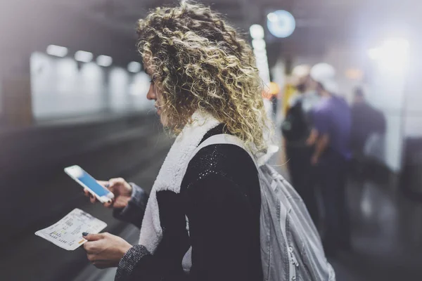Mujer atractiva con mochila en la plataforma de tránsito utilizando el teléfono inteligente para hacer foto del billete de tren mientras espera tren en la estación de metro . —  Fotos de Stock