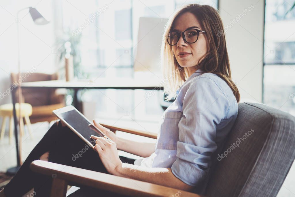 Handsome young blonde wearing glasses and using electronic touch tablet computer on sunny workplace.Horizontal. Blurred background.