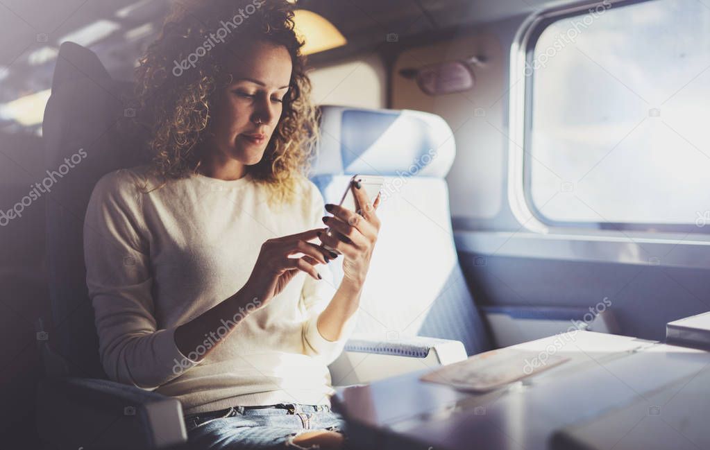 Enjoying travel concept. Young pretty woman tourist traveling by the train sitting near the window using smartphone.