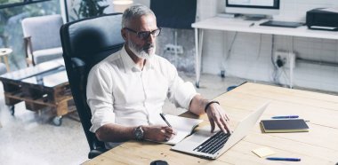 Modern coworking evinde ahşap masada otururken mobil dizüstü bilgisayar kullanan olumlu yetişkin iş adamı. Geniş.