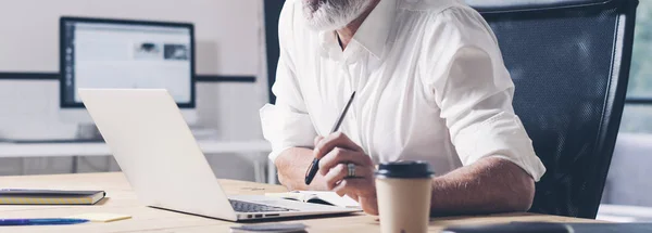 Nadenkend zakenman werken bij moderne naaiatelier kantoor. Zelfverzekerde man met behulp van de hedendaagse mobiele laptop. Wide.Cropped. — Stockfoto