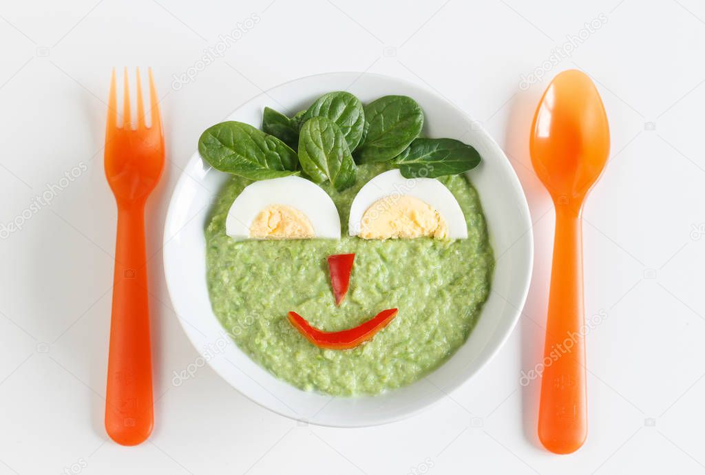Bowl of pureed green vegetables for baby with happy face made by egg and vegetables