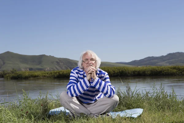 Uomo anziano seduto su una riva del fiume — Foto Stock