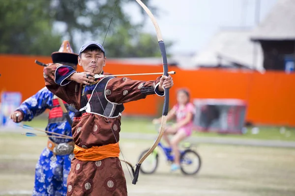 Competitions in shooting from a sports bow in Siberia. Mongolian competitions in archery. The sportsman is dressed in a traditional Buryat-Mongolian suit, shooting with his arrows during a national holiday.