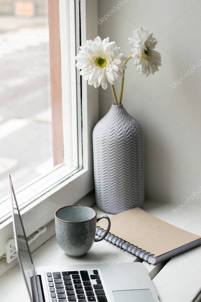 Bright workplace by the window with flowers, laptop, notebook and coffee cup