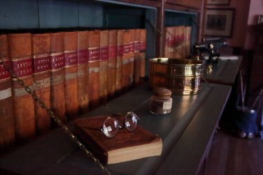 Eski kitaplarla dolu raflar. Kitapta gözlük var. Bir İngiliz kır evinde klasik stil.