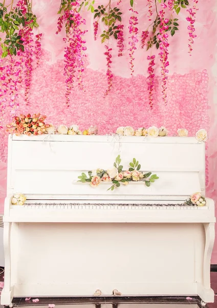 Piano branco em um fundo de flores rosa — Fotografia de Stock