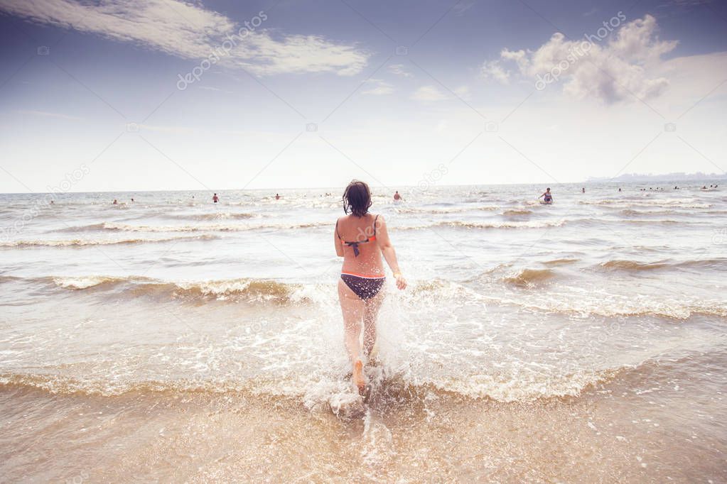 young woman runs into the sea spray flying