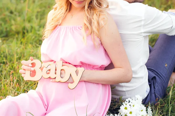 O rótulo "Baby" nas mãos de uma mulher grávida sentada atrás — Fotografia de Stock
