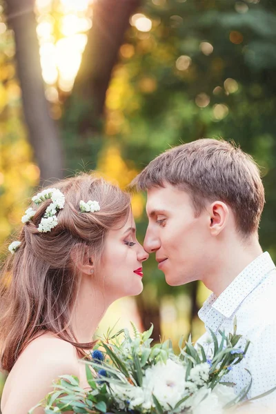 快乐的年轻新婚夫妇触摸鼻子在公园里 抱着一束 — 图库照片