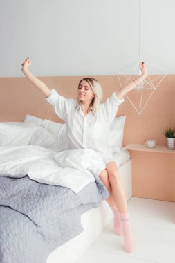 Genç kadın onun yatağında gülümseme ile oturuyor germe