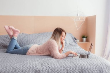 Şoförünün yatakta yatan bir dizüstü bilgisayar üzerinde çalışan mutlu rahat güzel kadın