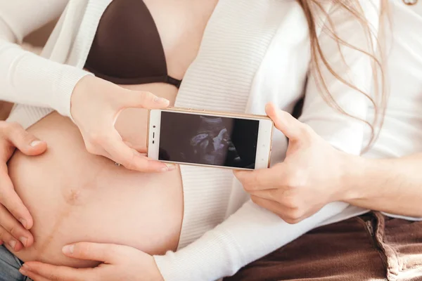 휴대폰 그들의 아기의 초음파 사진을 보여주는 사랑에 부부를 닫습니다 — 스톡 사진