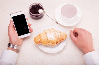 Kruvasan ile ahududu reçeli, kakao bir kupa, elinde telefon pho