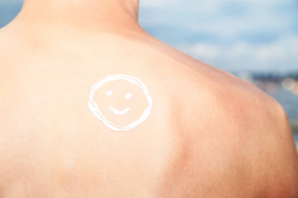 Lotion man met zonnebrandcrème smiley boven zee achtergrond — Stockfoto