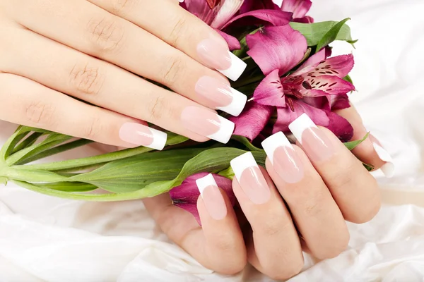 Manos con uñas manicuradas francesas sobre fondo de flores de lirio —  Fotos de Stock