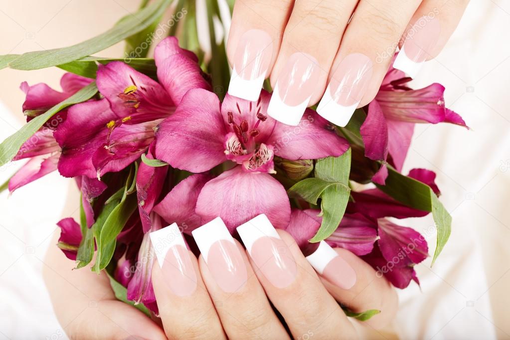 Hands with long artificial french manicured nails and lily flowers 
