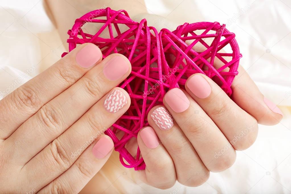 Hands with pink matte manicured nails holding a heart