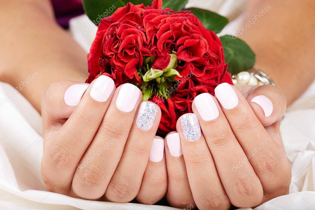 Hands with short manicured nails holding a red rose flower
