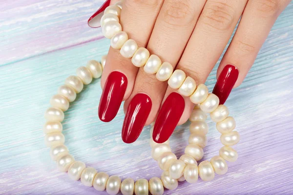 Mão com unhas longas e artificiais manicure coloridas com esmalte vermelho — Fotografia de Stock