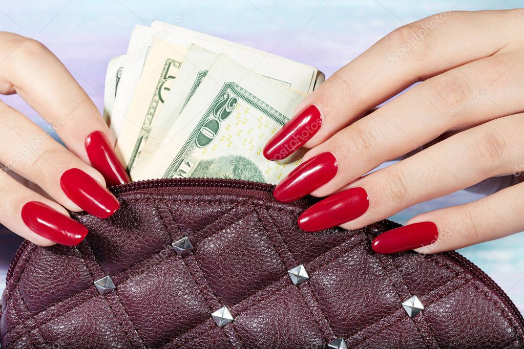 Hands with long artificial manicured nails taking out money from the handbag