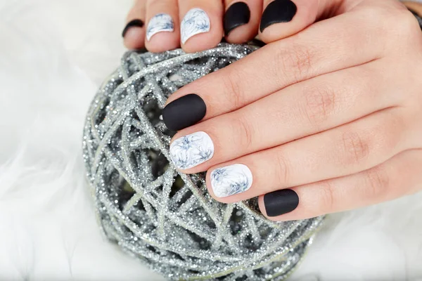 Hands with short manicured nails colored with black and white nail polish