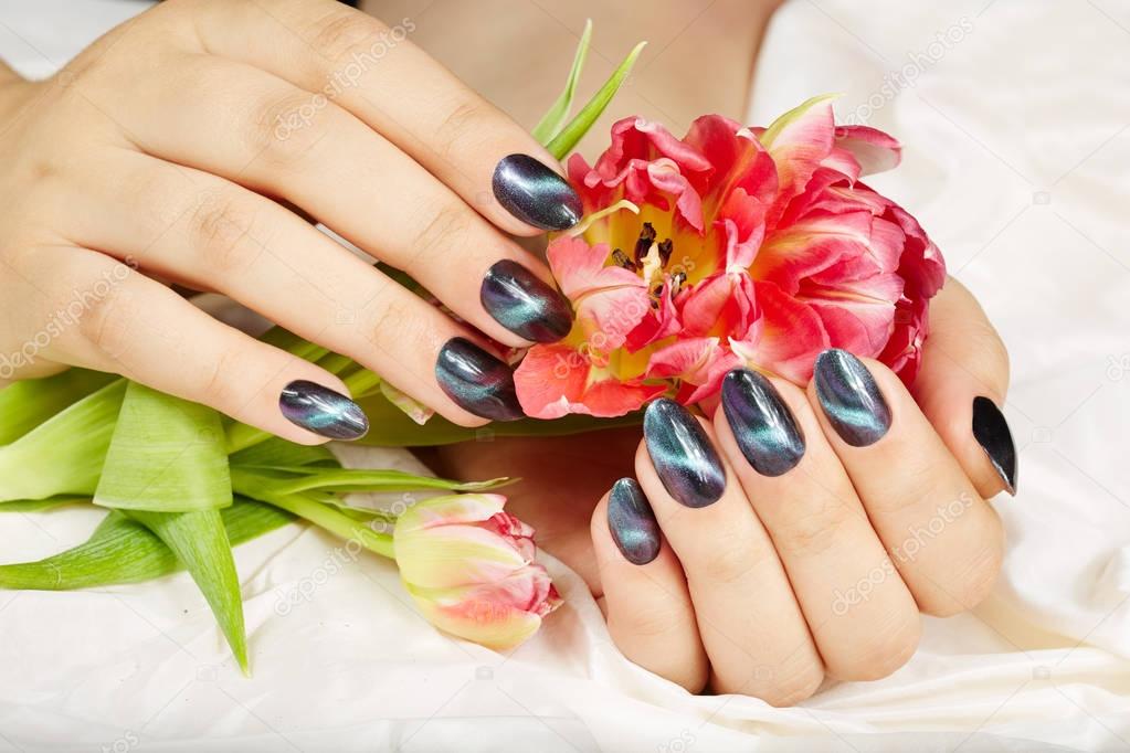 Hands with manicured nails with cat eye design holding pink tulip flower