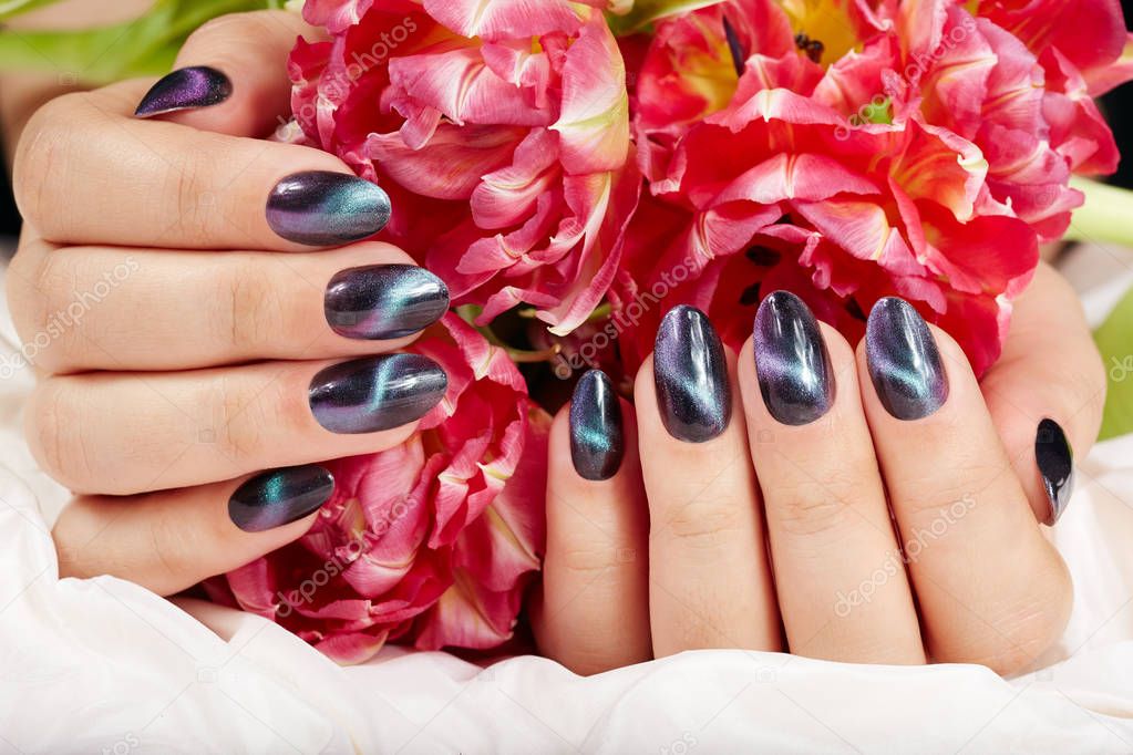 Hands with manicured nails with cat eye design holding pink tulip flowers