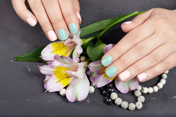 Hands with short manicured nails colored with pink and green nail polish and lily flowers