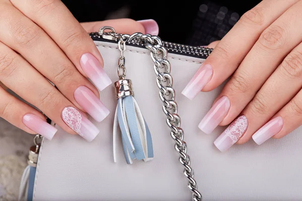 Hands with long artificial manicured nails with ombre gradient design in pink and white colors