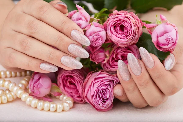 Hands with long artificial manicured nails colored with nail polish with silver glitter and pink roses
