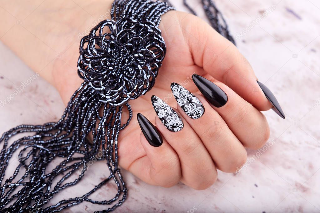 Hand with long artificial manicured nails colored with black nail polish and a necklace with flower
