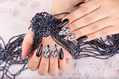 Hands with long artificial manicured nails colored with black nail polish and a necklace with flower