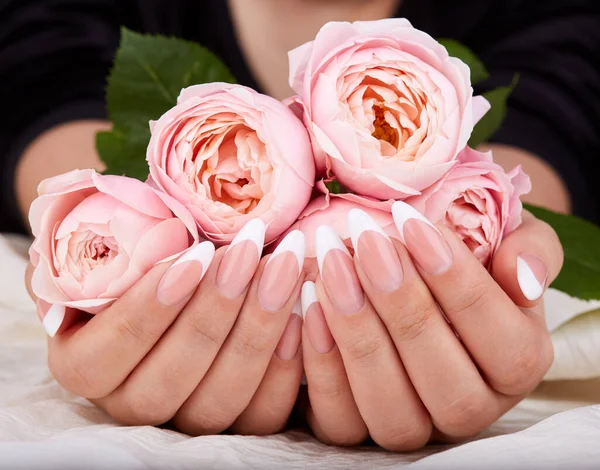 Uzun, yapay, manikürlü ve elinde pembe gül çiçekleri olan eller.
