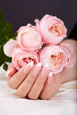 Uzun, yapay, manikürlü, pembe gül çiçekleri tutan bir el.